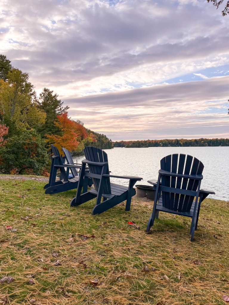 Blue Muskoka Chairs on Oak Lake at The Trace wellness and leisure resort in Ontario with Fall leaves in the background.